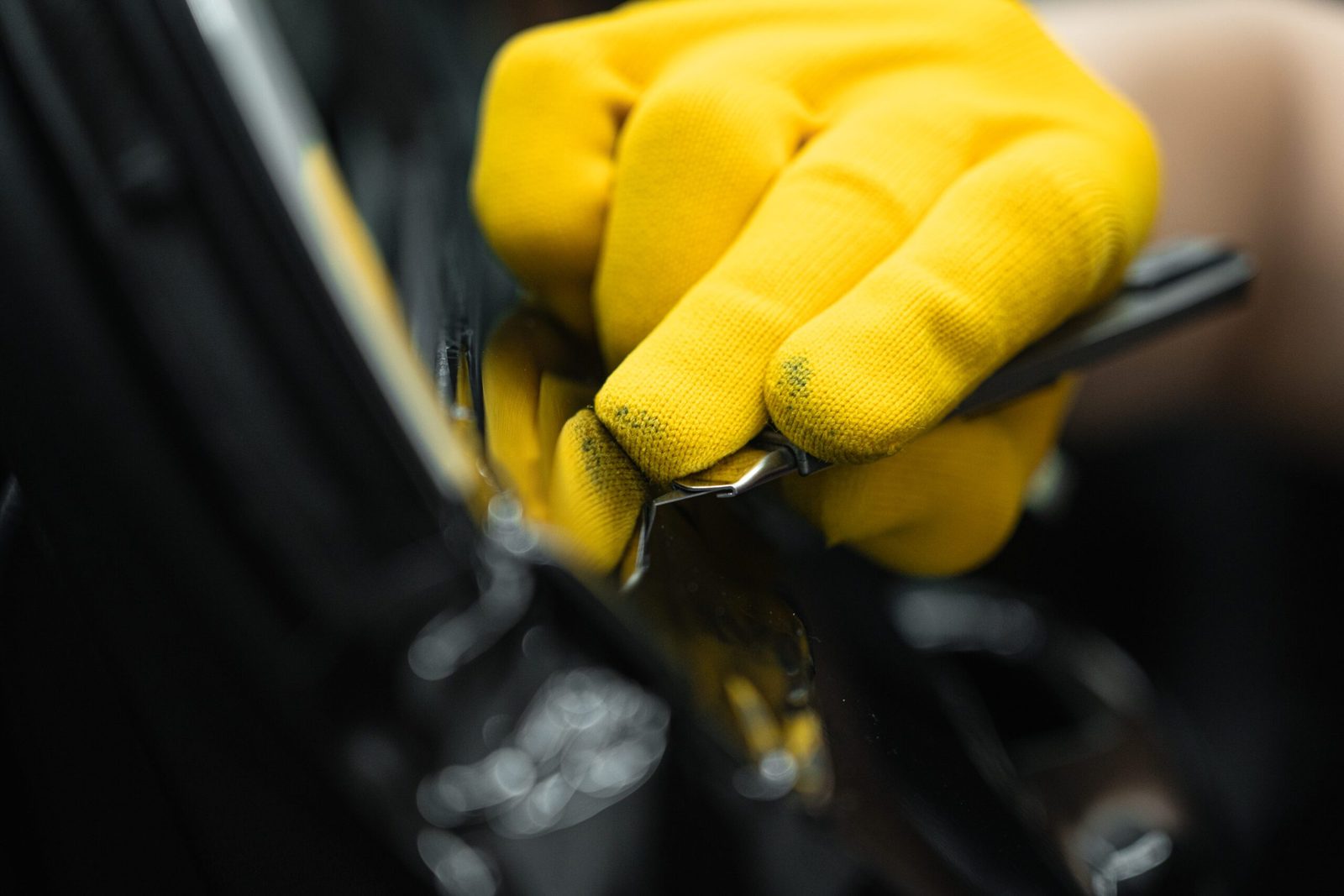 Gele handschoen wrijft een donkere lak uit langs de portierrand