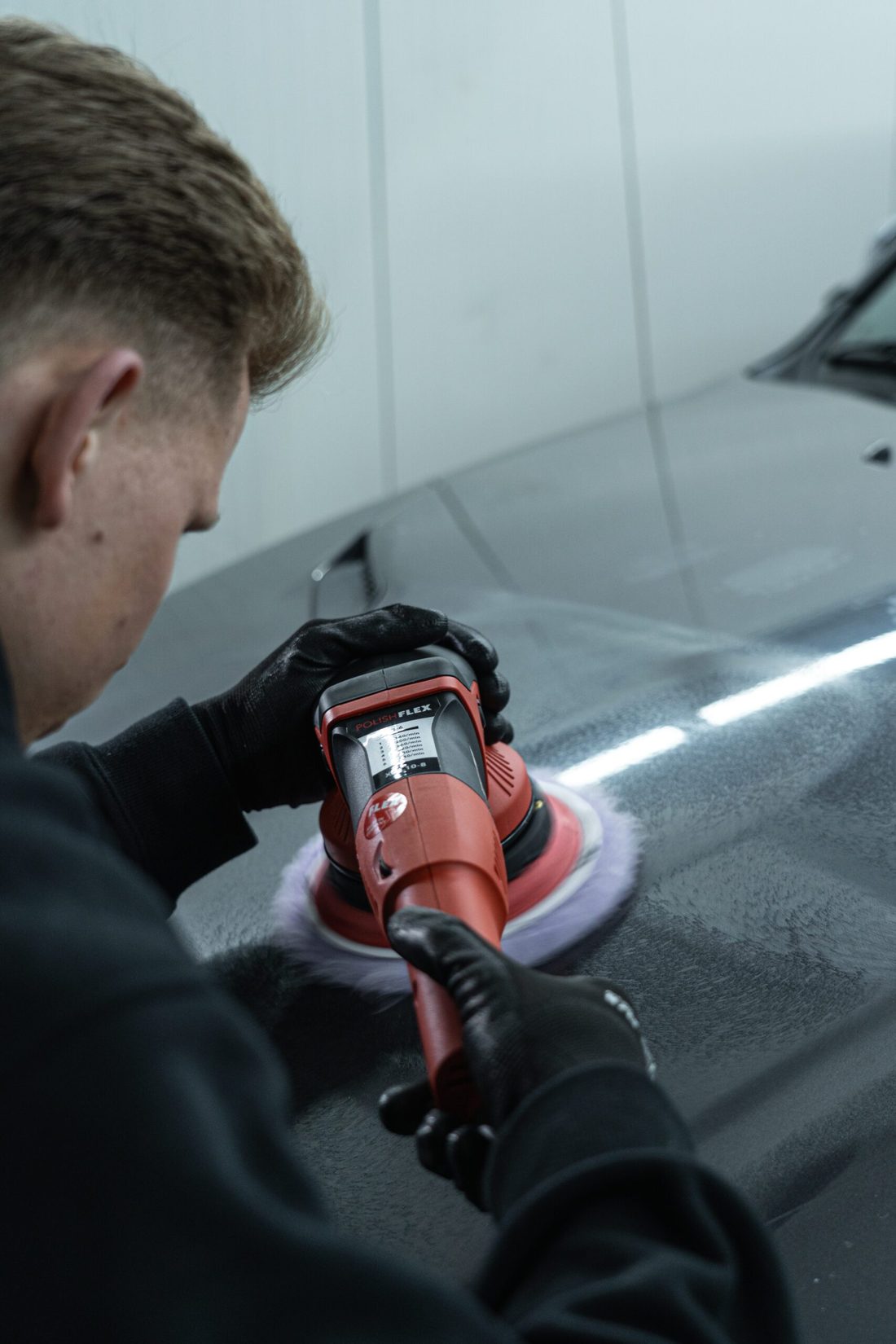 Polijstmachine op een donkere motorkap onder het lichtplafond
